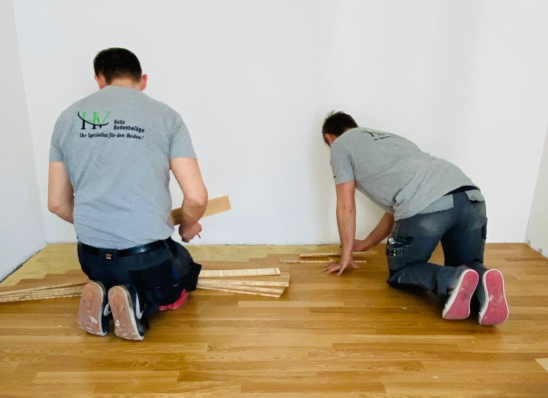 Zwei Mitarbeiter von HoVa Bodenbeläge verlegen Parkett an einer Wand